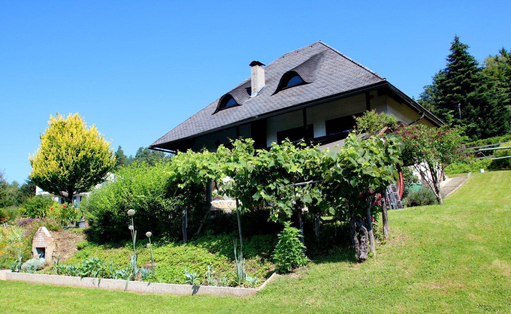 Haus mit Satteldach und weitläufigem, terrassiertem Gartenbereich mit Weinreben.