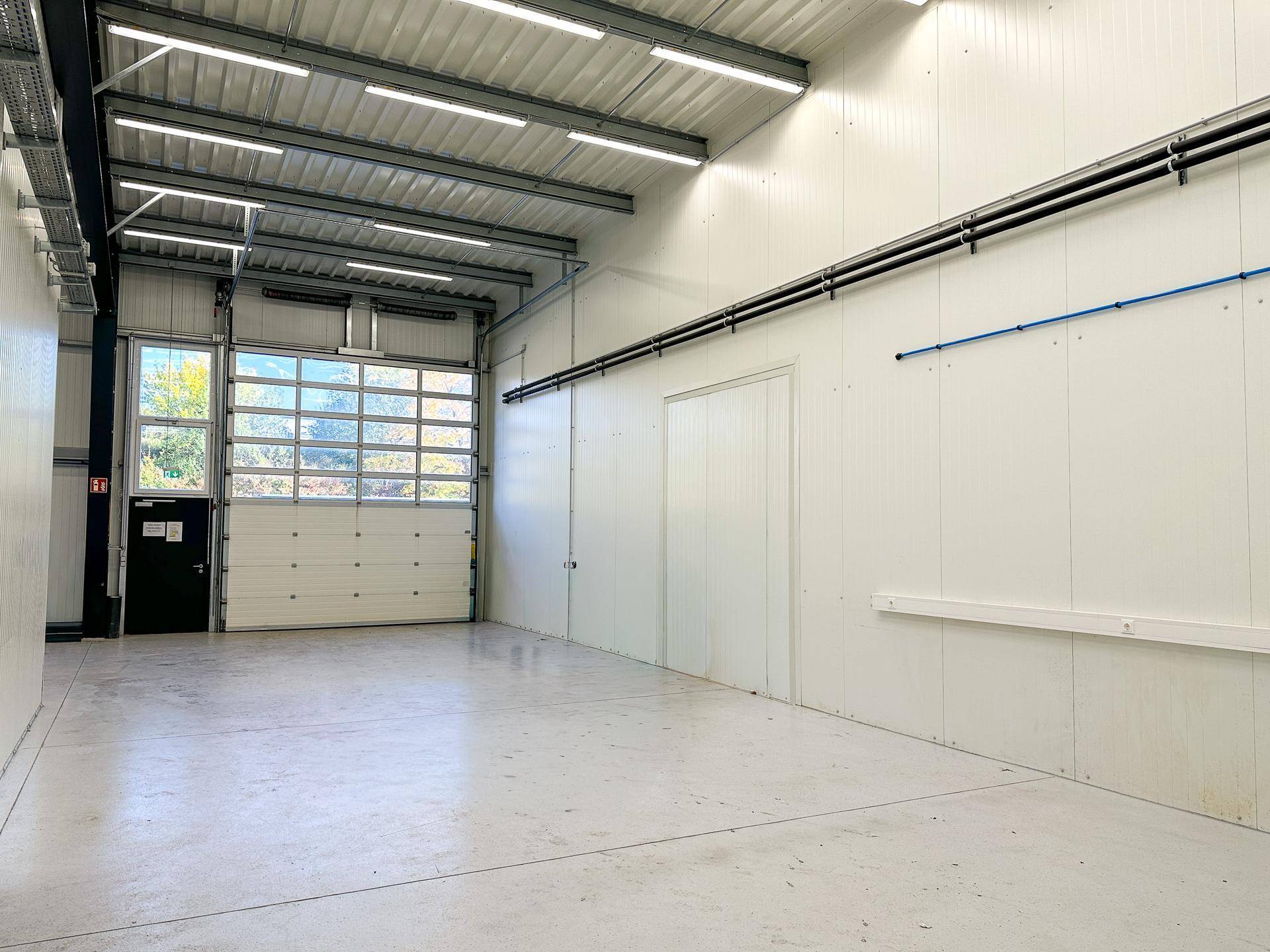 Geräumige, leere Lagerhalle mit hoher Decke, Betonboden und großem Sektionaltor für den Zugang.