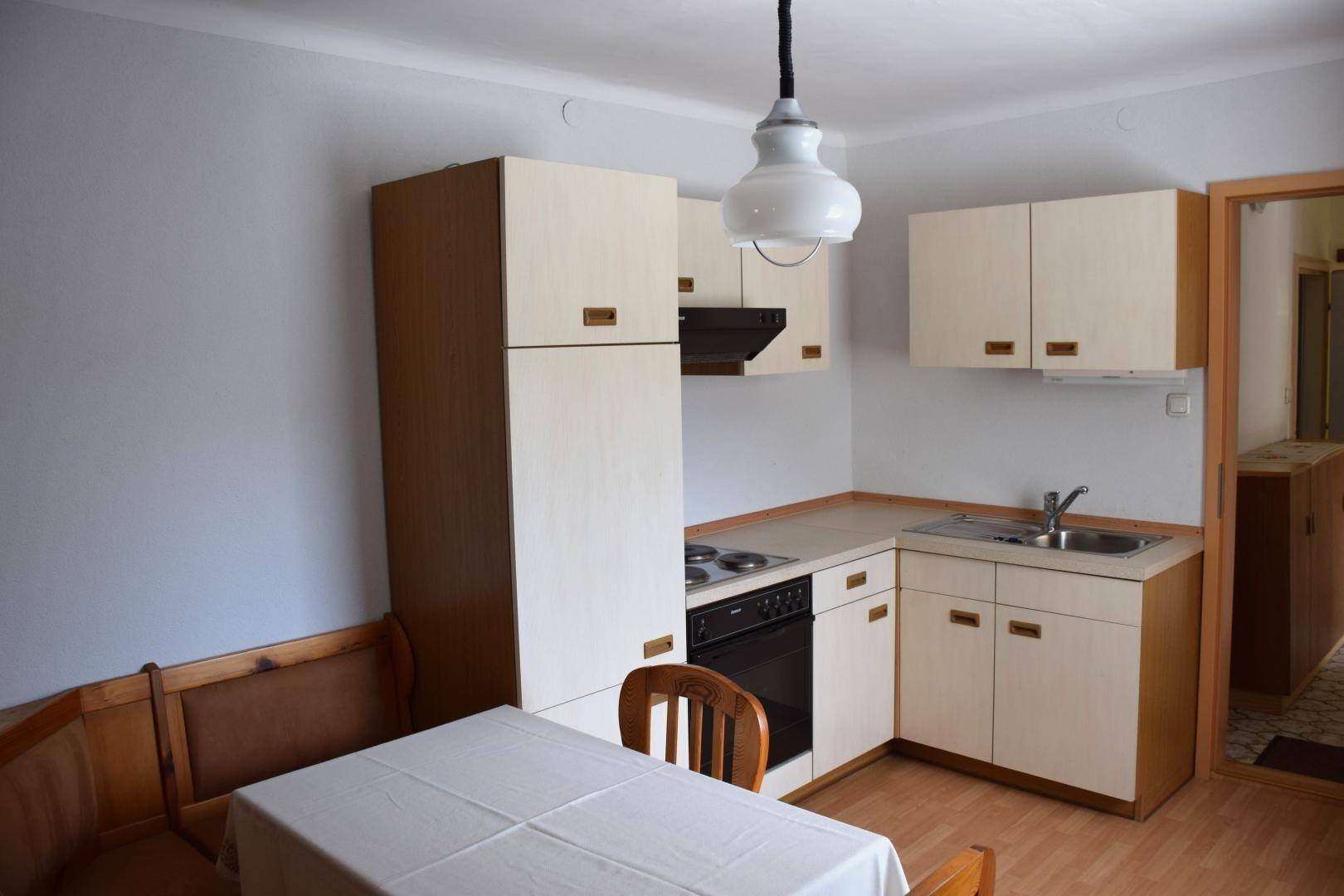 Kleine Küche mit Essbereich, älteren Einbaumöbeln und Holzbank.