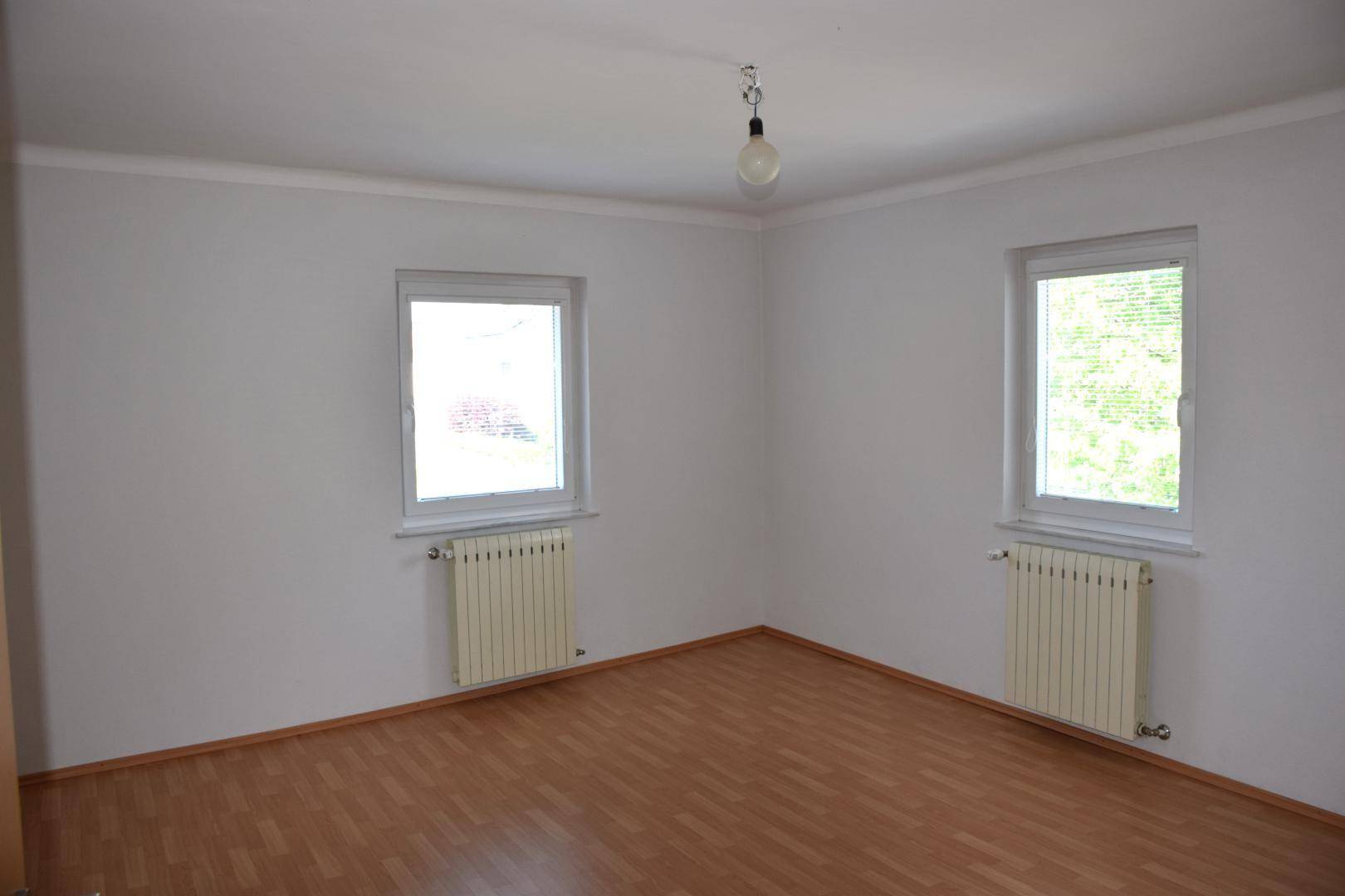 Leeres Zimmer mit zwei Fenstern, Heizkörpern und Laminatboden.
