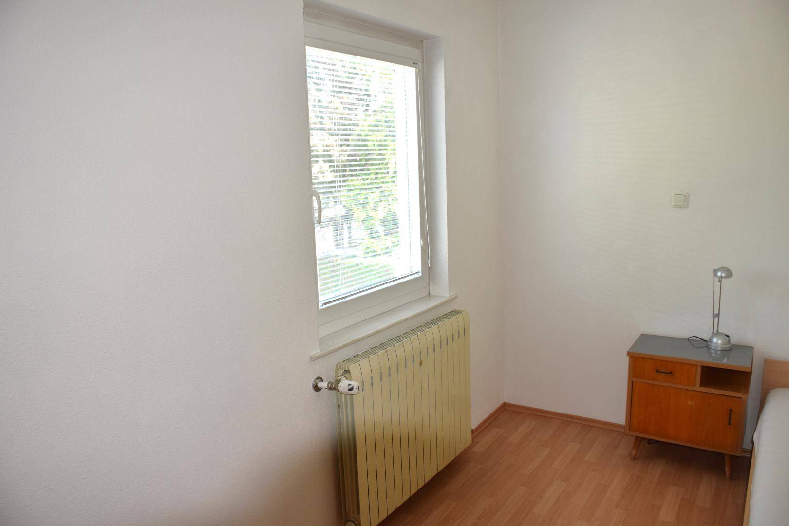 Schlafzimmer mit einem Fenster, Heizkörper und kleinem Nachttisch.
