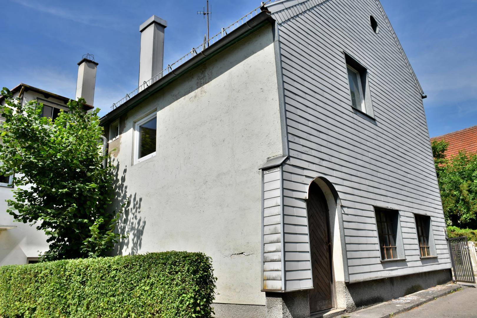 Seitenansicht des Wohnhauses mit Holzverkleidung und gepflegter Hecke im Vorgarten.
