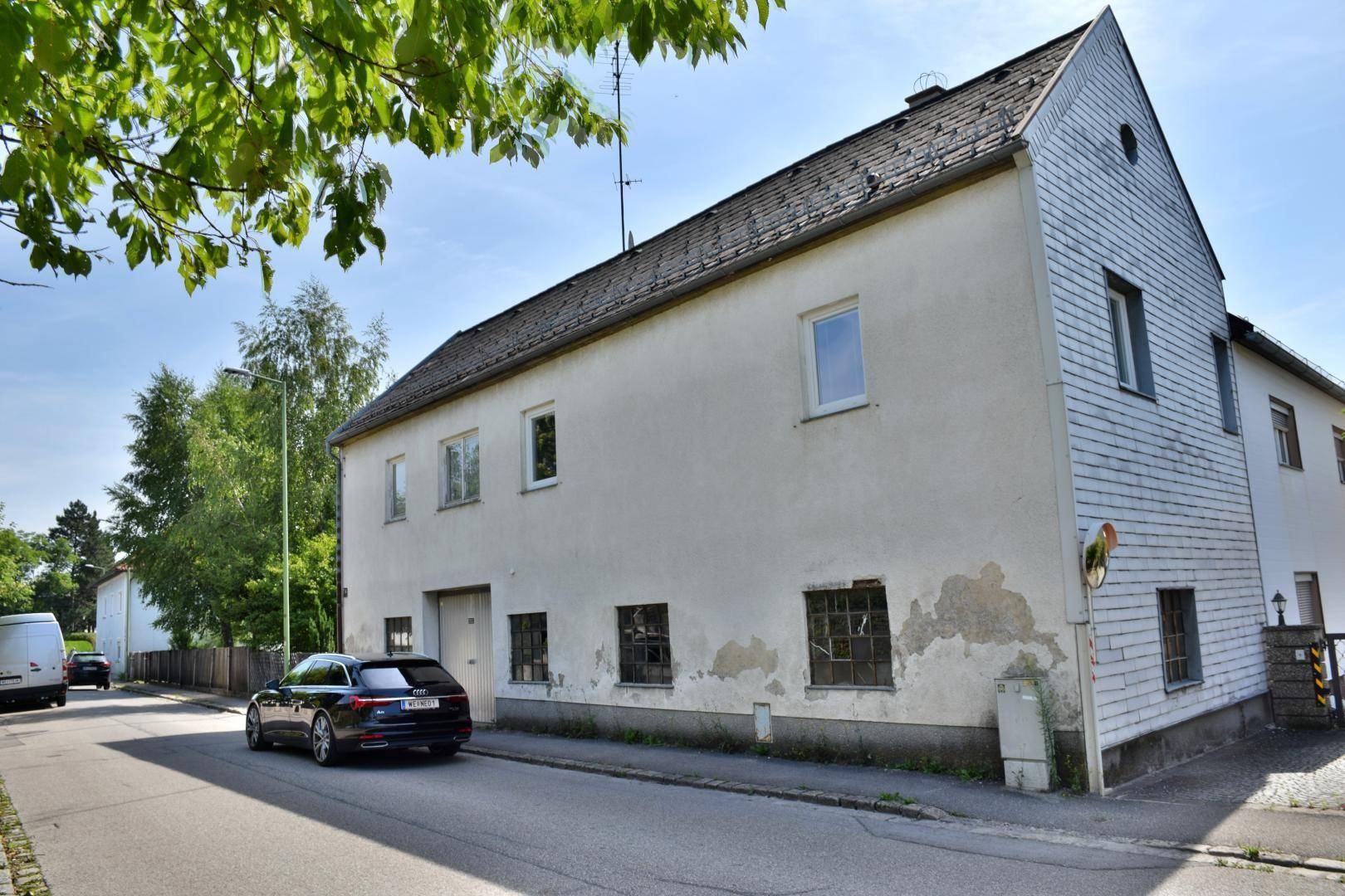 Ansicht des Wohnhauses von der Straße mit geparktem Auto und grüner Umgebung.