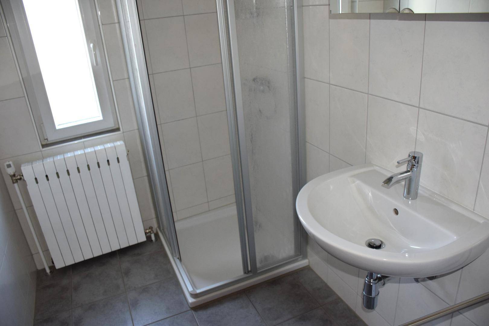 Badezimmer mit Duschkabine, Einzelwaschbecken und Fenster.