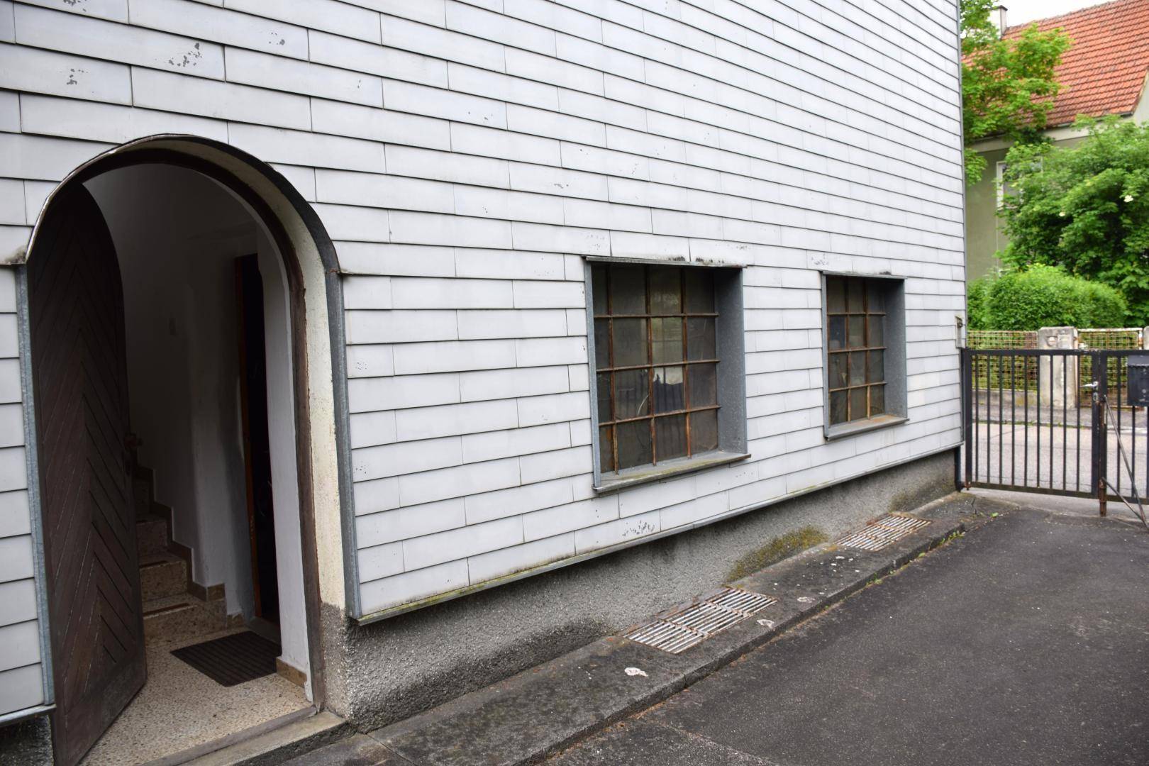Eingangsbereich des Hauses mit gewölbter Tür und vergitterten Fenstern an der Seitenfassade.
