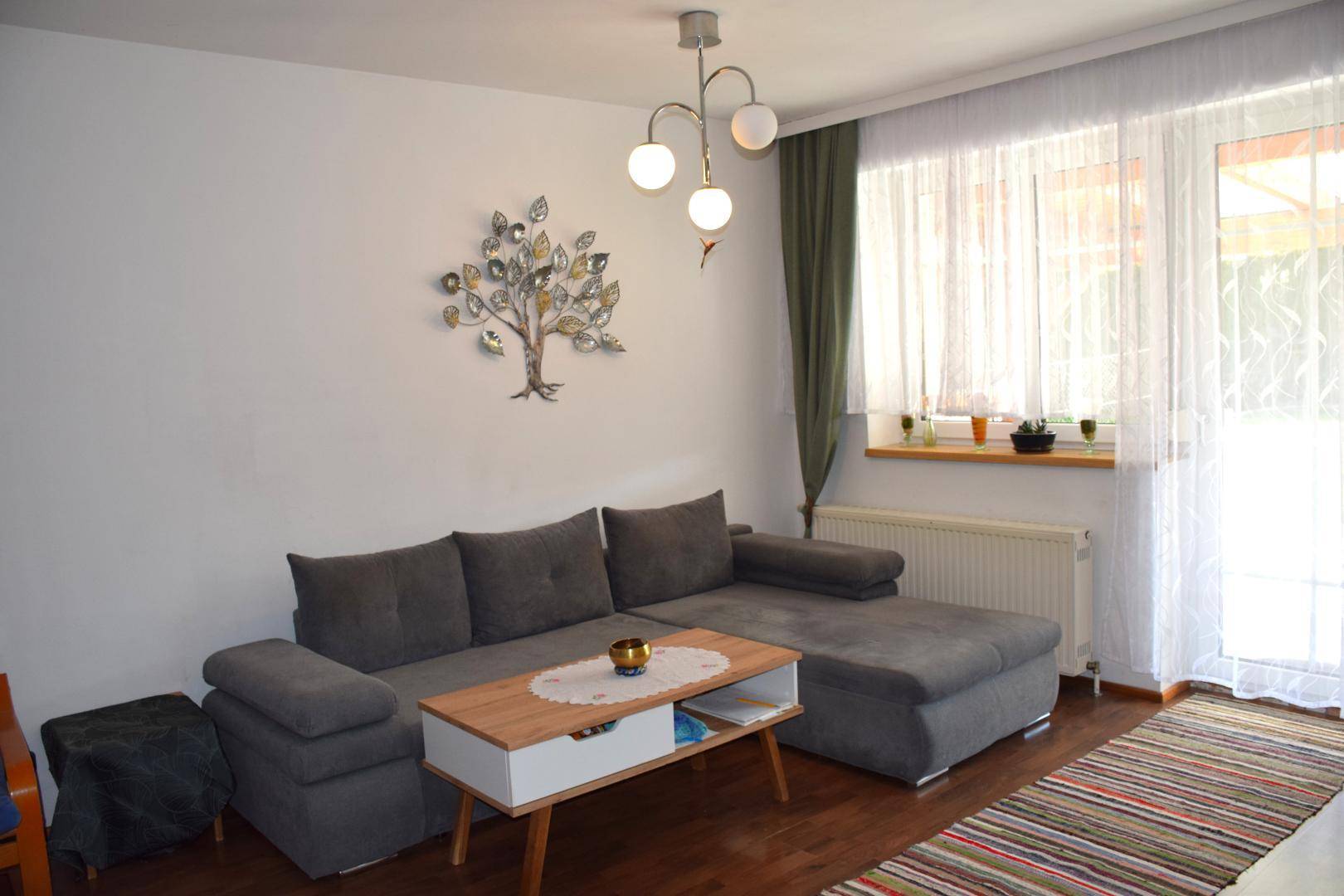 Helles Wohnzimmer mit modernem Sofa, Holzboden und Zugang zu einem Außenbereich.