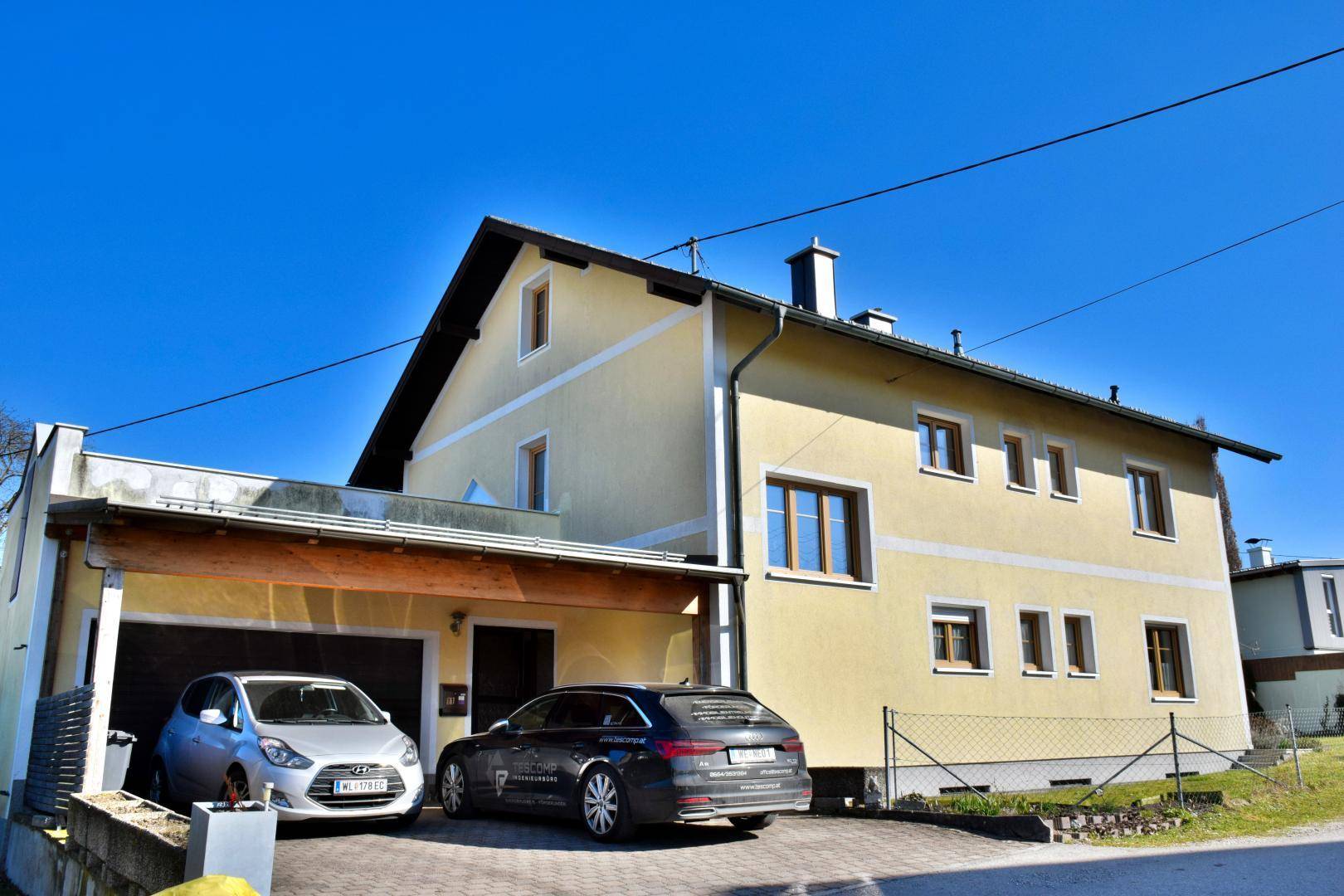 Seitenansicht des Hauses mit integrierter Garage und gepflasterter Einfahrt.