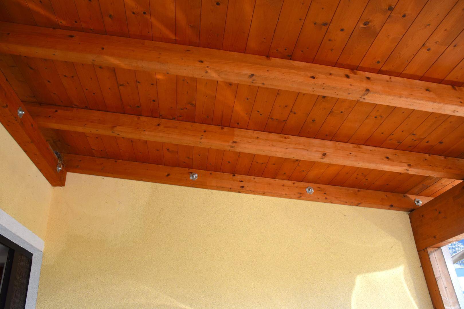 Holzdecke der überdachten Terrasse mit sichtbaren Balken und eingelassenen Lichtern.
