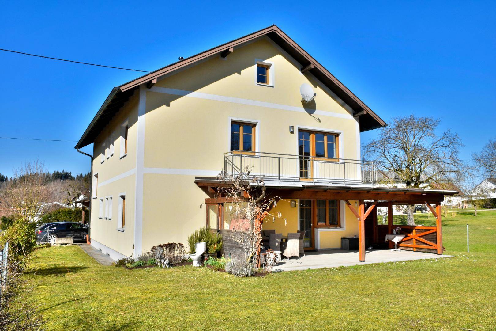Ansicht des Zweifamilienhauses mit gepflegtem Garten und überdachter Terrasse im Sonnenschein.