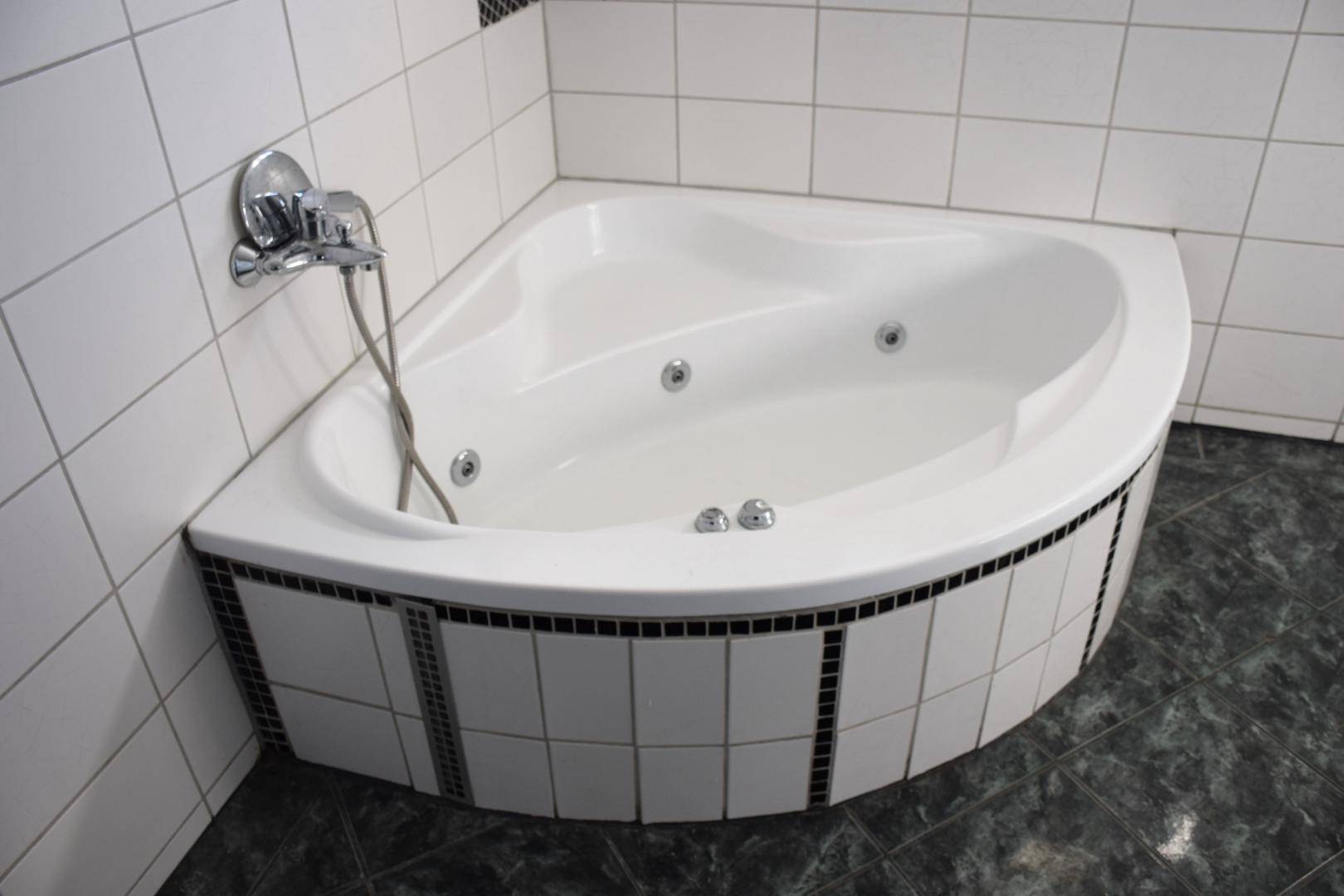 Eckbadewanne mit integrierten Whirlpooldüsen in einem gefliesten Badezimmer.