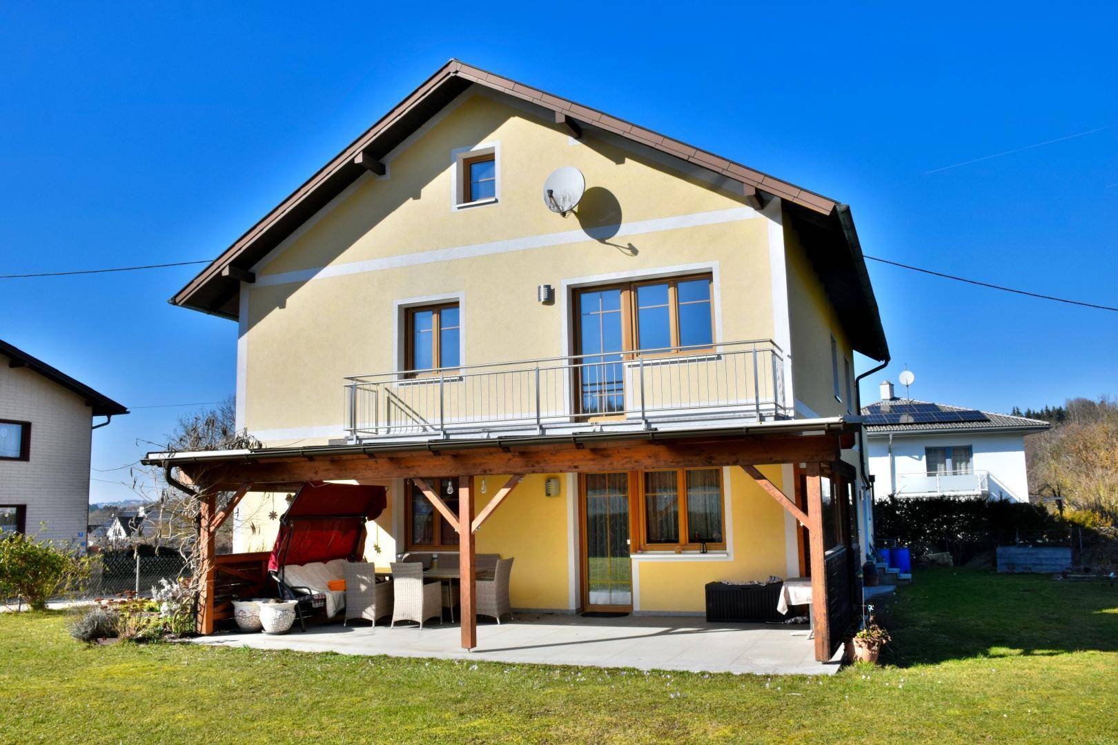Rückansicht des Hauses mit großer überdachter Terrasse und Blick ins Grüne.