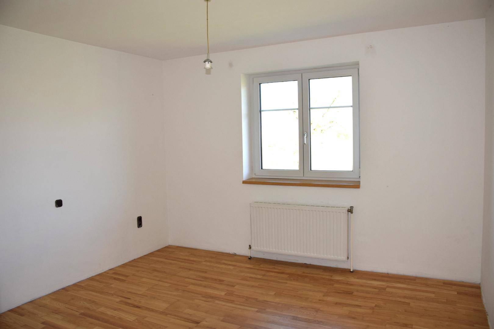 Helles Schlafzimmer mit Parkettboden, weißen Wänden und großem Fenster.