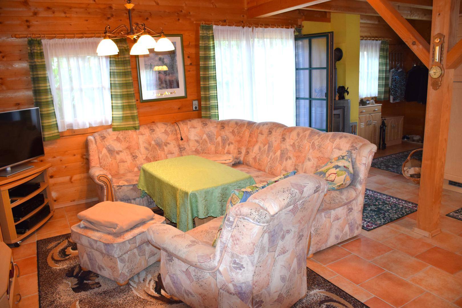 Rustikales Wohnzimmer mit bequemer Eckcouch, Holzvertäfelung und Fliesenboden.