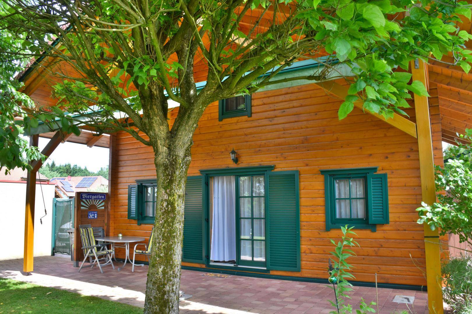 Gemütliche Terrasse unter einem Baum am Holzhaus, ideal für entspannte Stunden im Freien.
