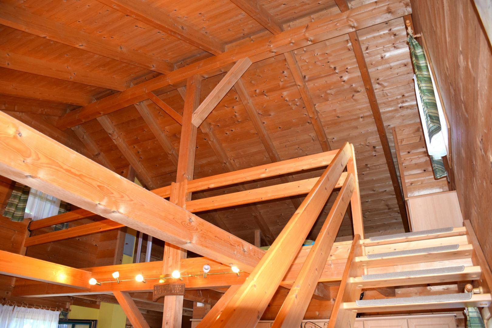 Offene Holztreppe führt zu einem oberen Bereich mit sichtbaren Dachbalken und Holzverkleidung.