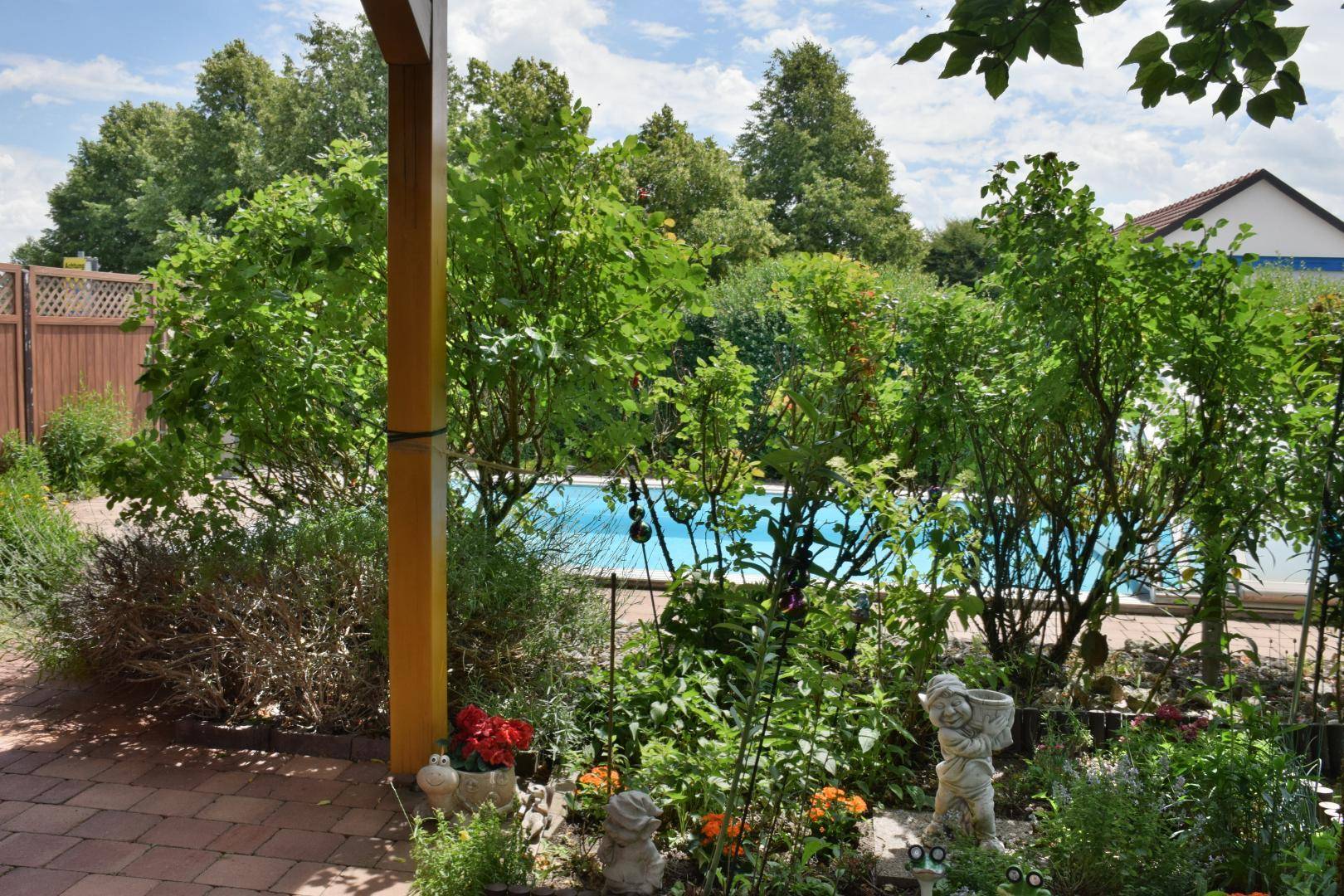 Üppiger Gartenbereich mit Blumenbeeten und einem Blick auf den dahinterliegenden Pool.