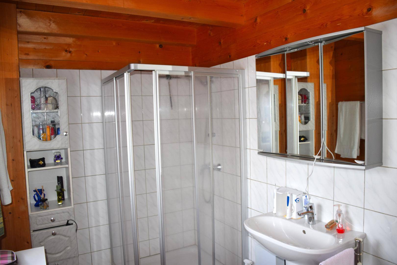 Badezimmer mit weiß gefliesten Wänden, Duschkabine und Waschbecken mit Spiegelschrank.