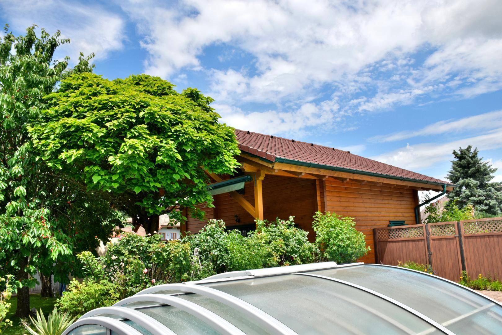 Gartenbereich mit üppigem Grün, Bäumen und der Abdeckung eines Pools unter blauem Himmel.
