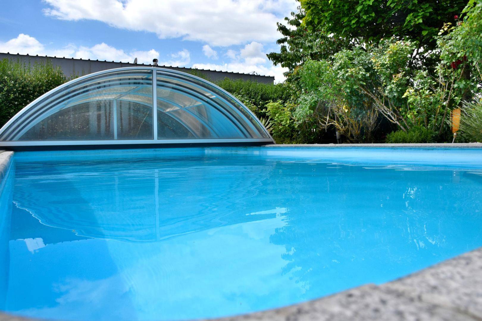 Nahaufnahme des blauen Swimmingpools mit seiner transparenten Abdeckung unter hellem Himmel.