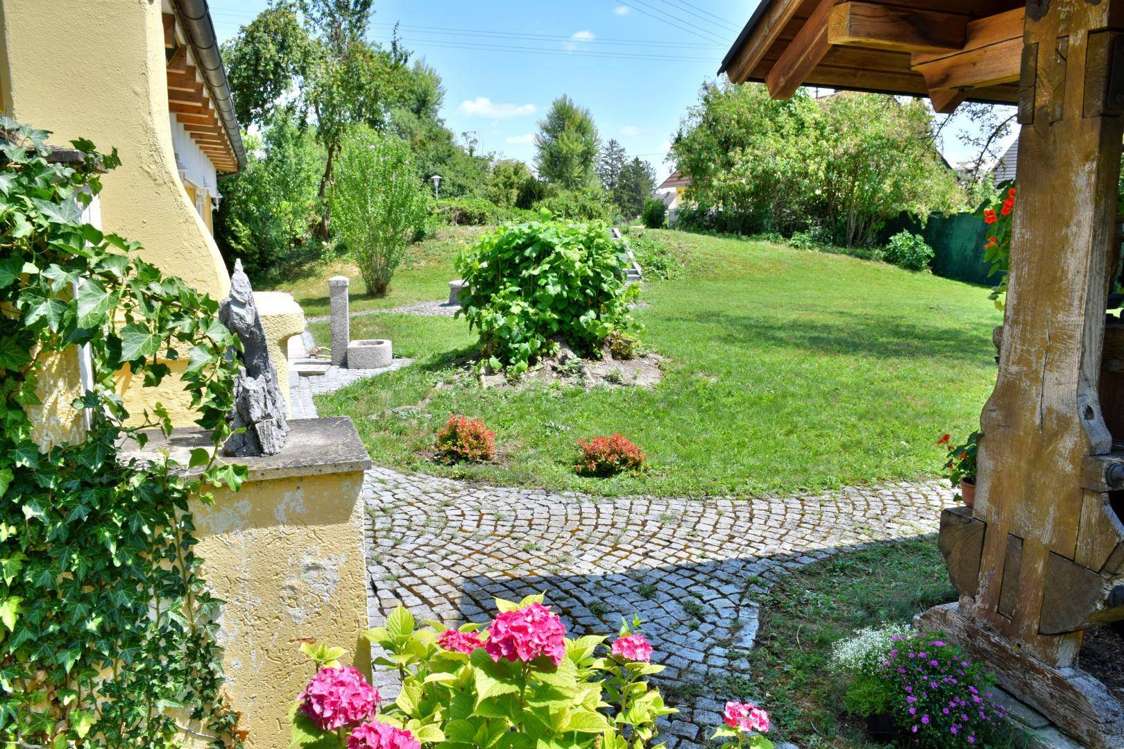 Blick in den grünen Garten mit gepflastertem Weg, blühenden Hortensien und einer sanften Rasenfläche.