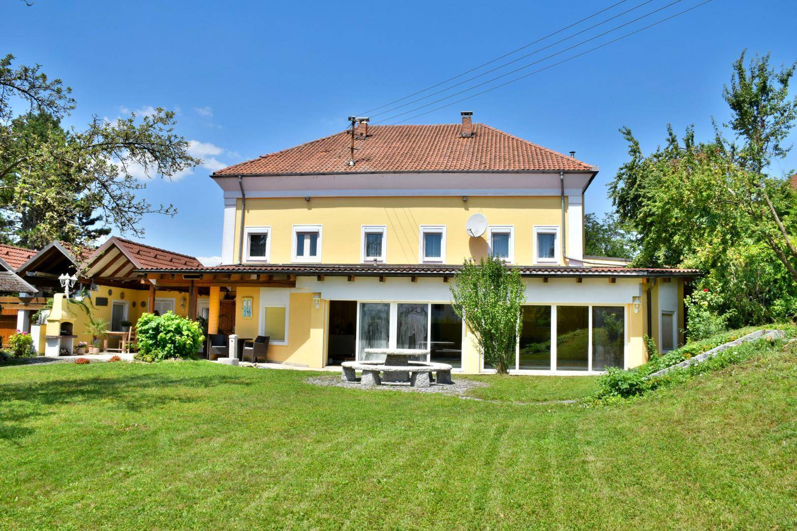 Großes gelbes Gebäude mit rotem Ziegeldach, umgeben von einem gepflegten grünen Garten mit Steintisch.