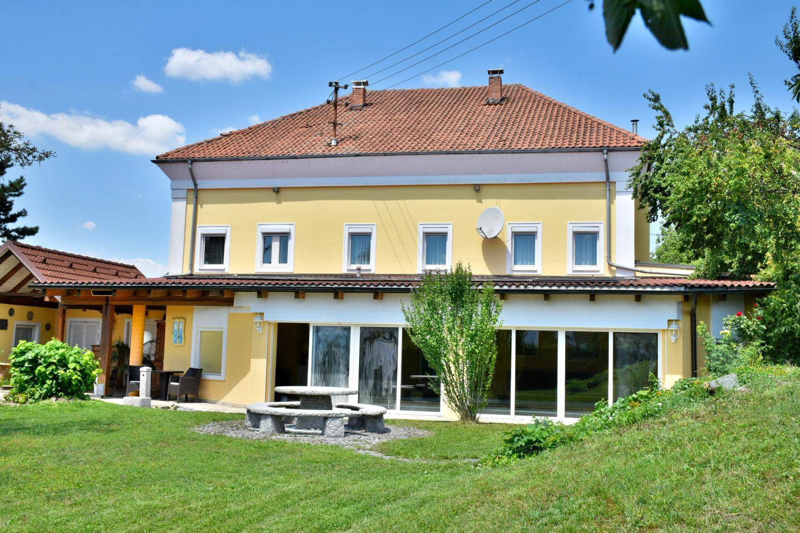 Ansicht des gelben Hauses mit großzügiger Rasenfläche und einem rustikalen Steintisch im Freien.