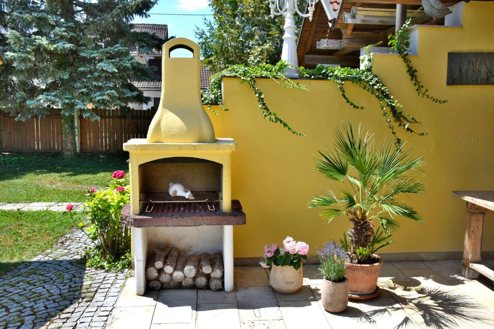 Detailansicht des gemauerten Grills auf der Terrasse mit Holzscheiten und dekorativen Pflanzen.