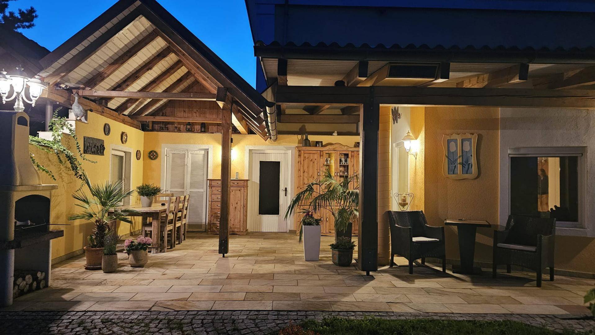 Die überdachte Terrasse bei Nacht, stimmungsvoll beleuchtet mit rustikalen Holzmöbeln und Grill.