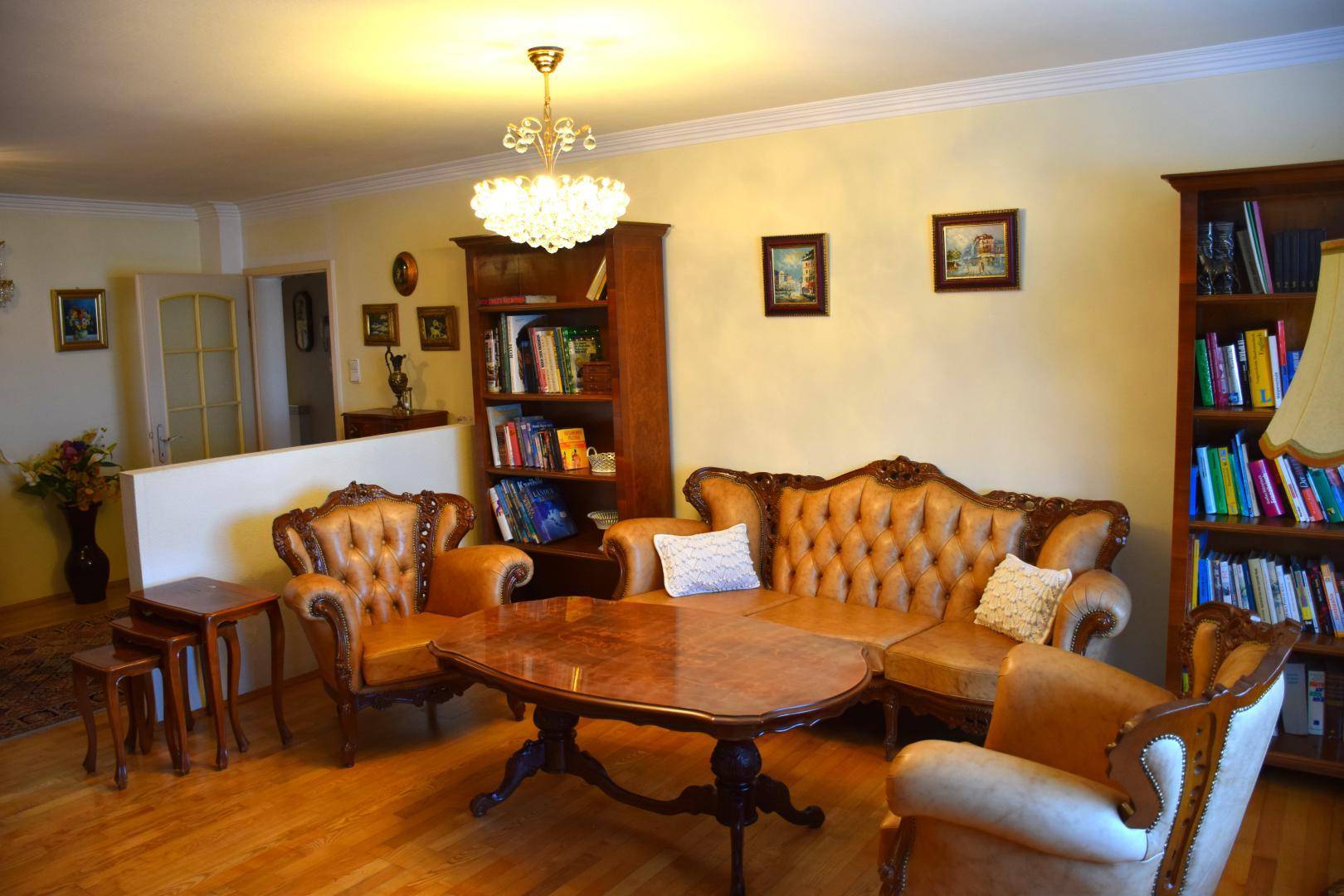 Klassisches Wohnzimmer mit Ledersofas, Holzbücherregalen und einem eleganten Couchtisch auf Parkettboden.