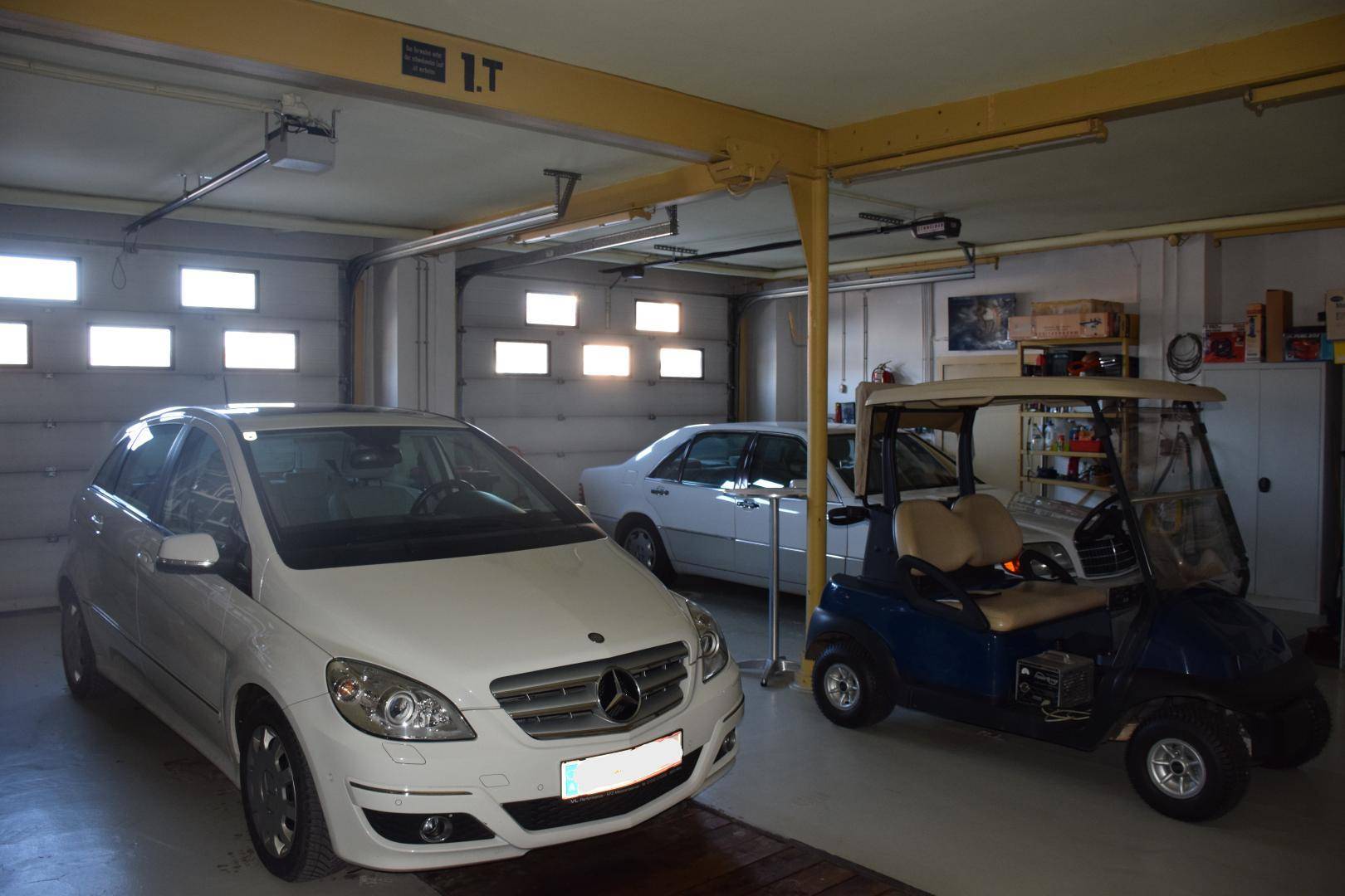 Helle Garage mit drei Fahrzeugen, darunter ein Golfwagen, und mehreren Garagentoren.