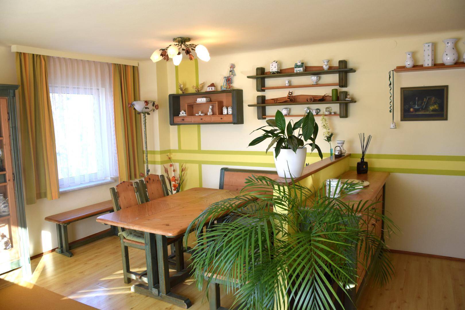 Gemütlicher Essbereich mit Holztisch und Bänken, farbigen Wänden und dekorativen Regalen.