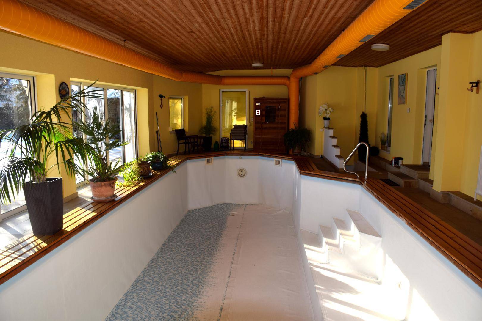 Großer Innenpoolbereich mit Holzdecke, großen Fenstern und einer sichtbaren Sauna im Hintergrund.