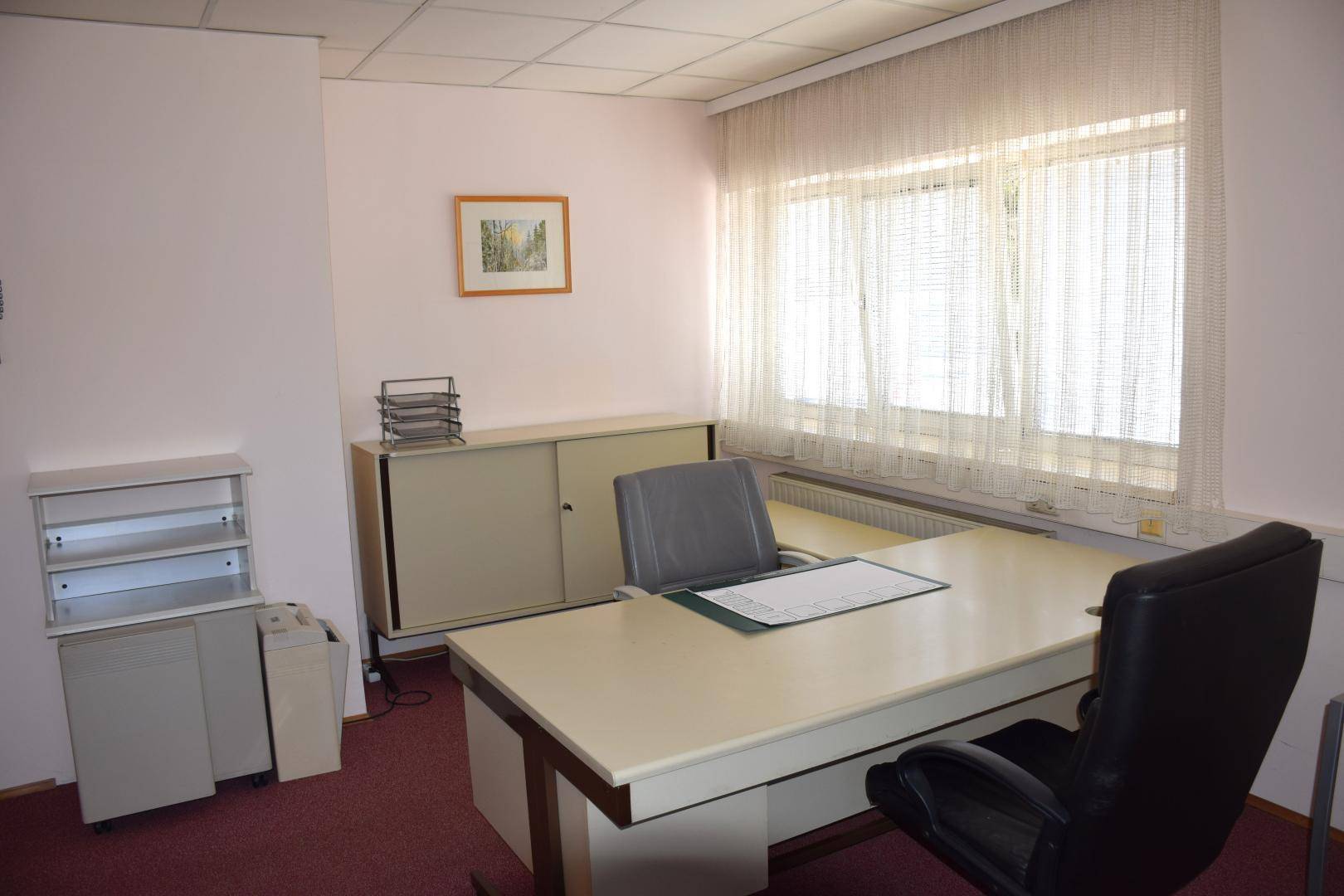 Büroraum mit großem Schreibtisch, Bürostühlen und Fenstern mit Vorhängen, ausgestattet für Arbeitszwecke.