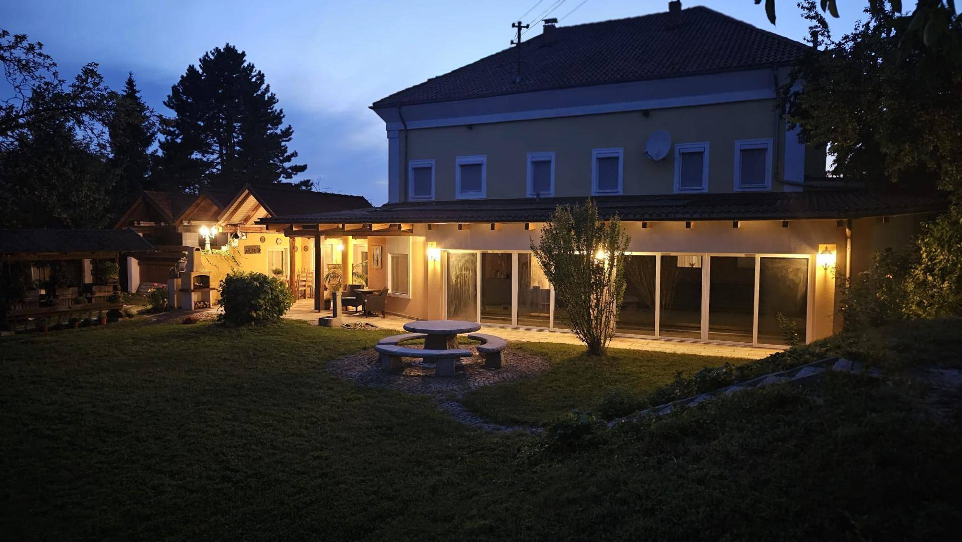 Das beleuchtete Gebäude und der Garten in der Abenddämmerung, mit gemütlicher Außenbeleuchtung.