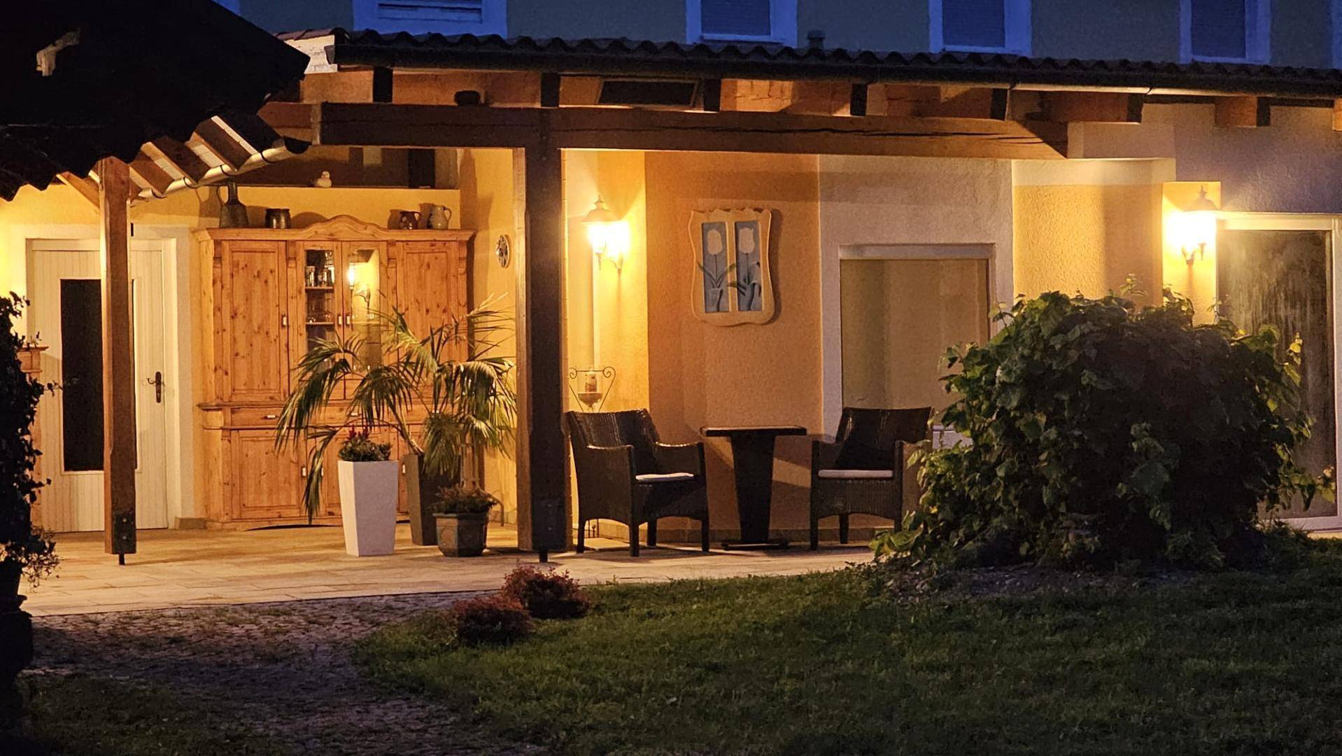 Gemütliche überdachte Terrasse am Abend, beleuchtet und mit bequemen Sitzgelegenheiten und Pflanzen.