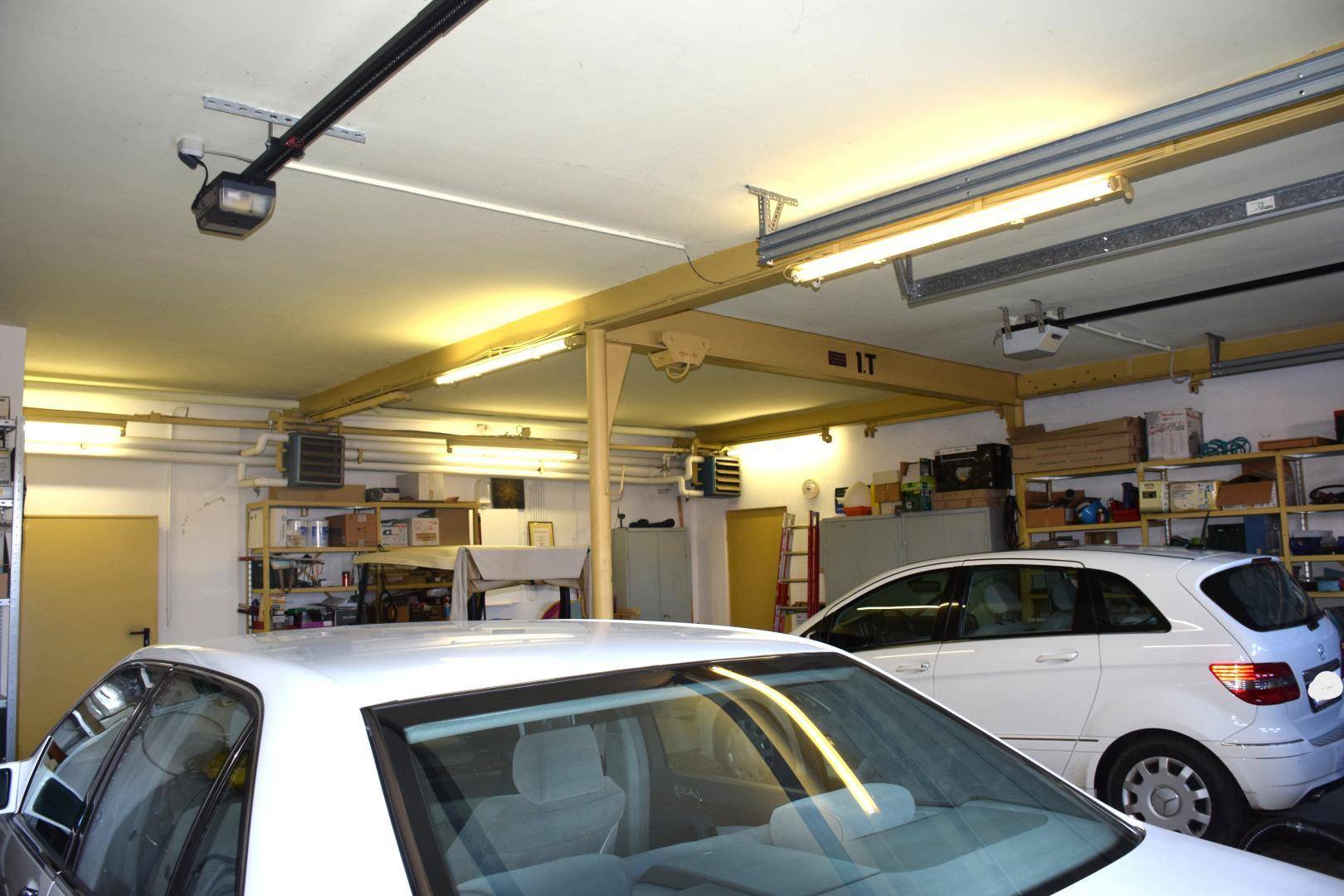 Geräumige Garage mit zwei Fahrzeugen, Regalen für Lagerung und heller Deckenbeleuchtung.
