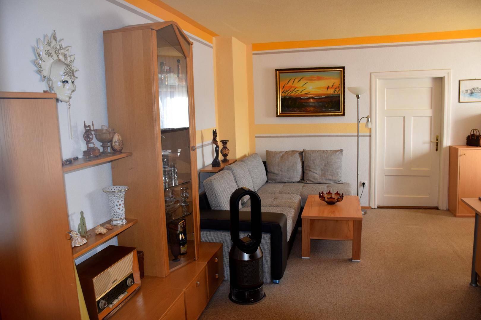 Modern eingerichtetes Wohnzimmer mit grauem Ecksofa, Holztisch und Teppichboden.