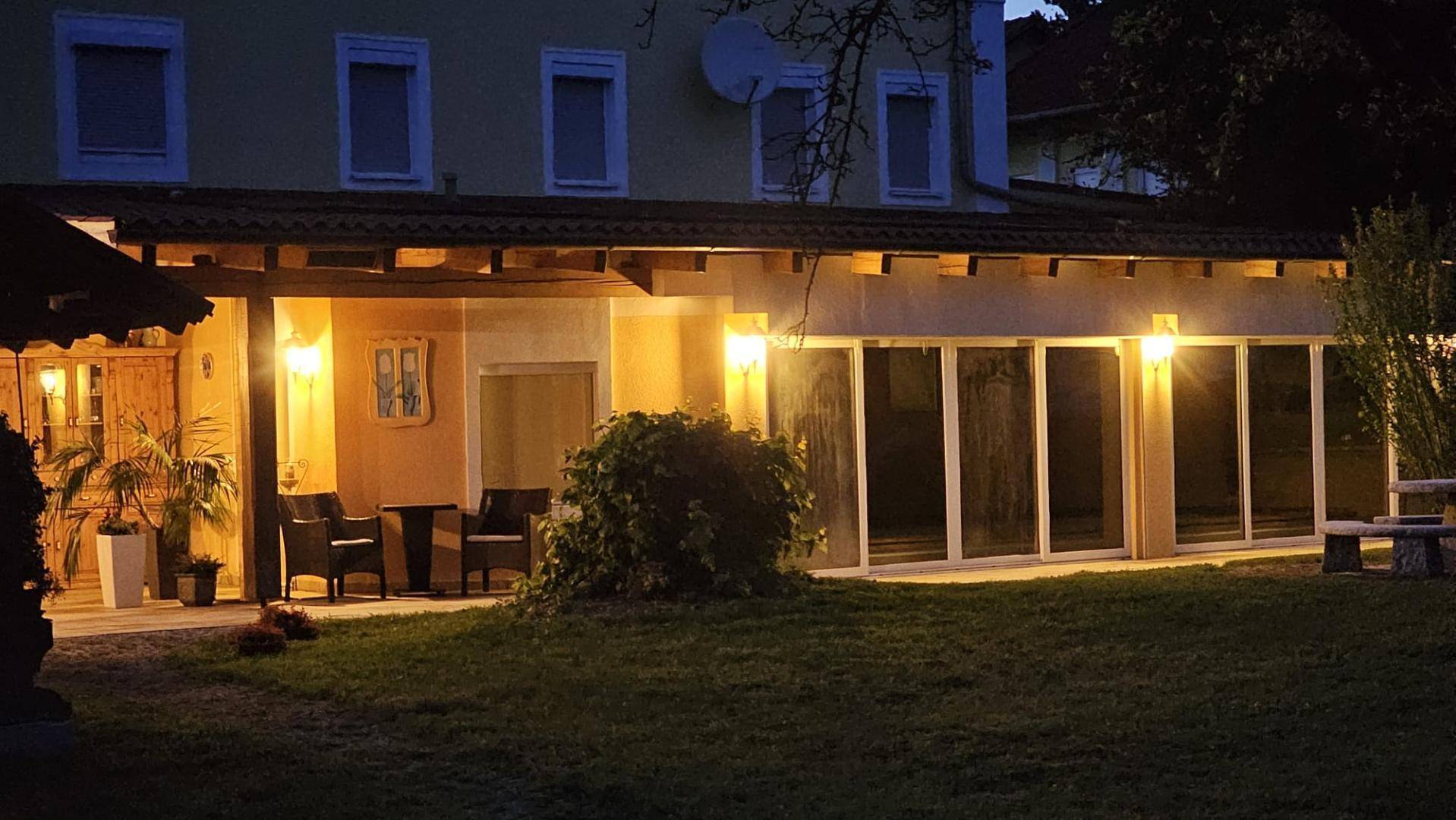 Das Gebäude und der Garten bei Nacht, mit beleuchteter Glasfassade und gemütlicher Terrasse.