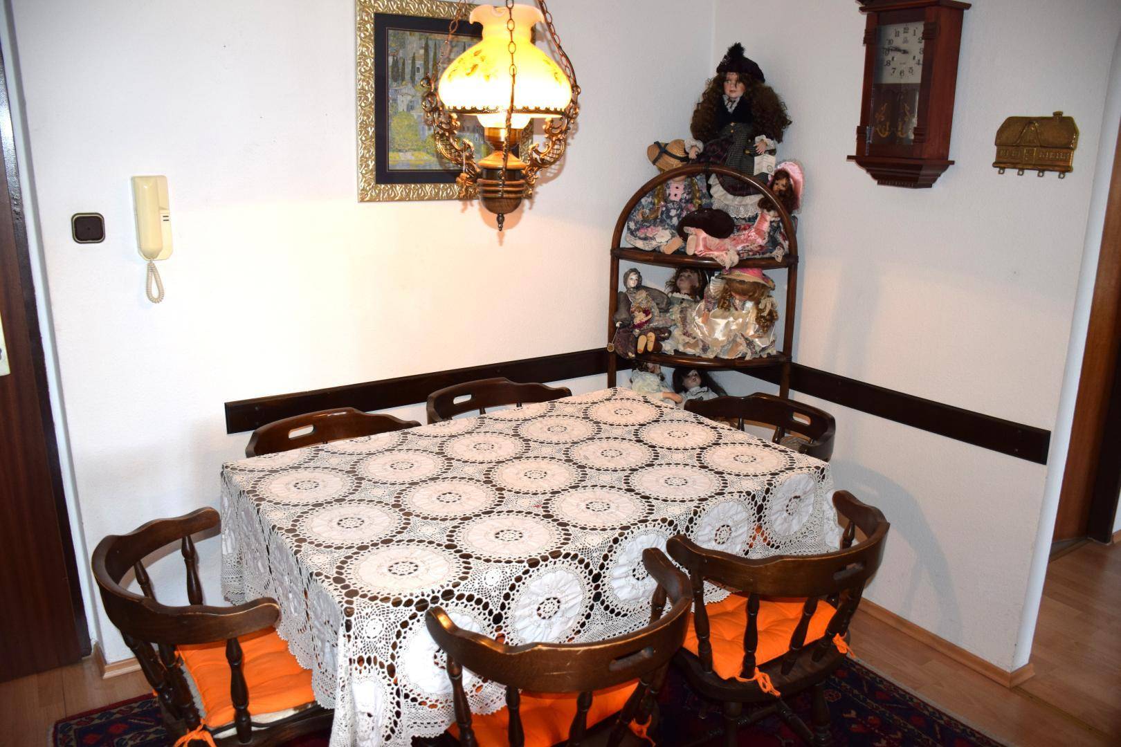 Essbereich mit Holztisch, Stühlen, Öllampe und einer Sammlung von Puppen auf einem Regal.