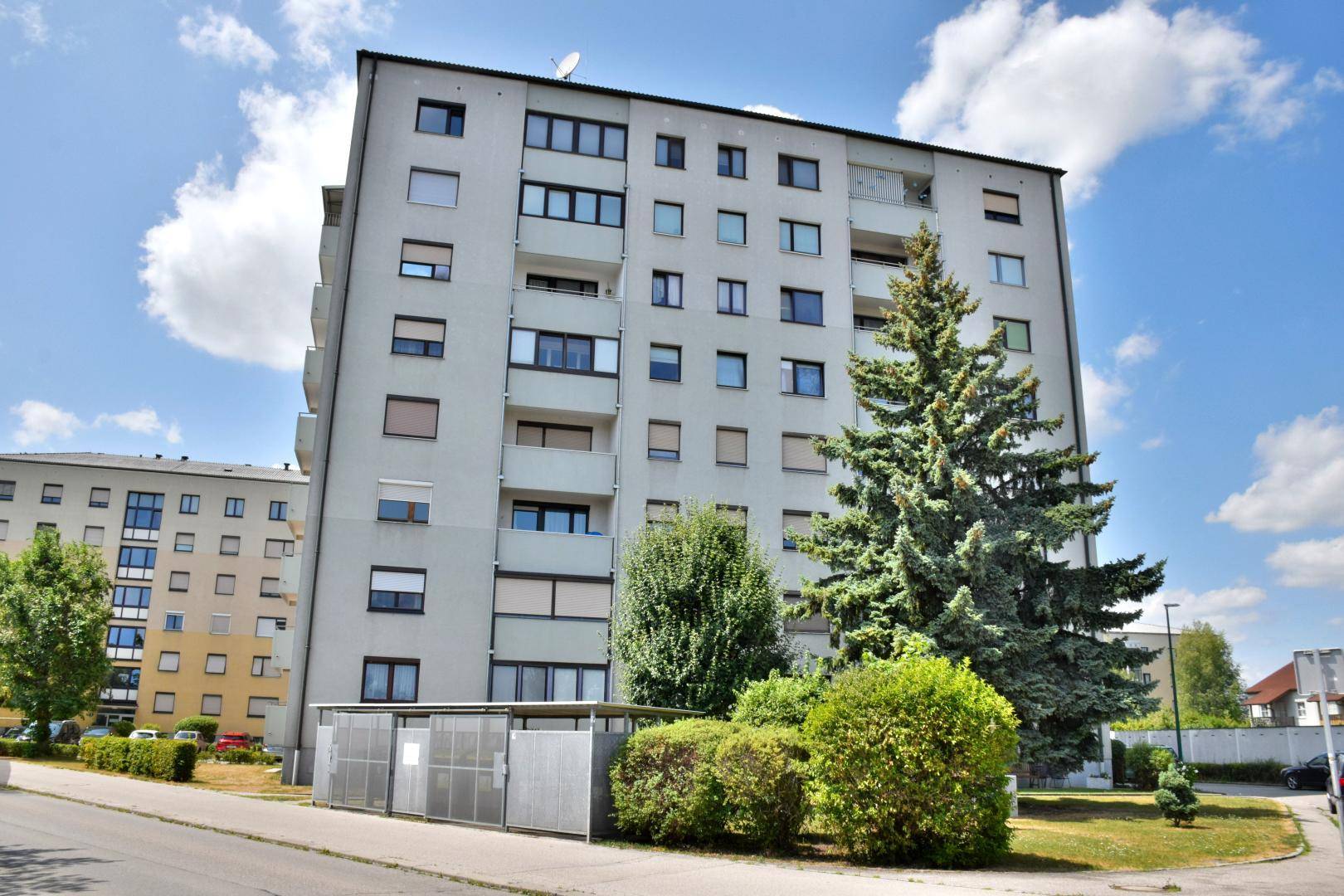 Mehrstöckiges Wohngebäude mit vielen Fenstern und Balkonen unter blauem Himmel.