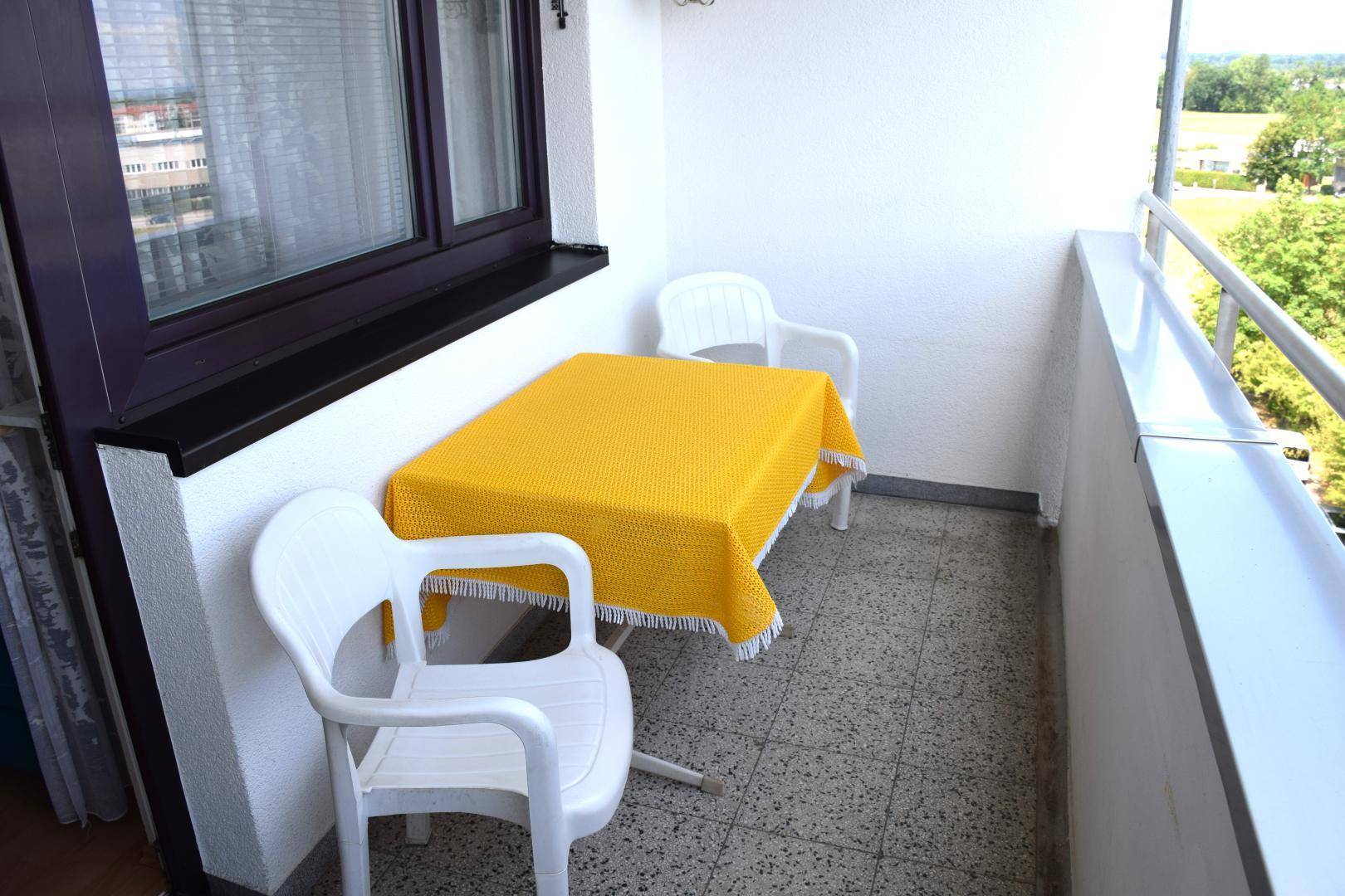 Kleiner Balkon mit Tisch und Stühlen, gefliestem Boden und Blick ins Grüne.