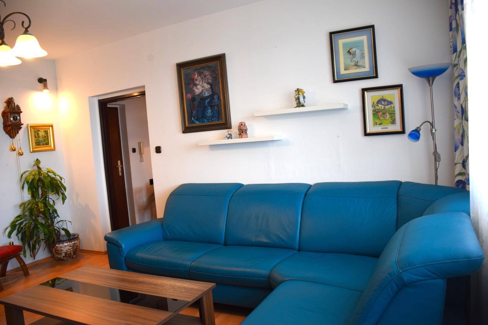 Gemütliches Wohnzimmer mit blauer Ledercouch, Holztisch und dekorativen Bildern an der Wand.
