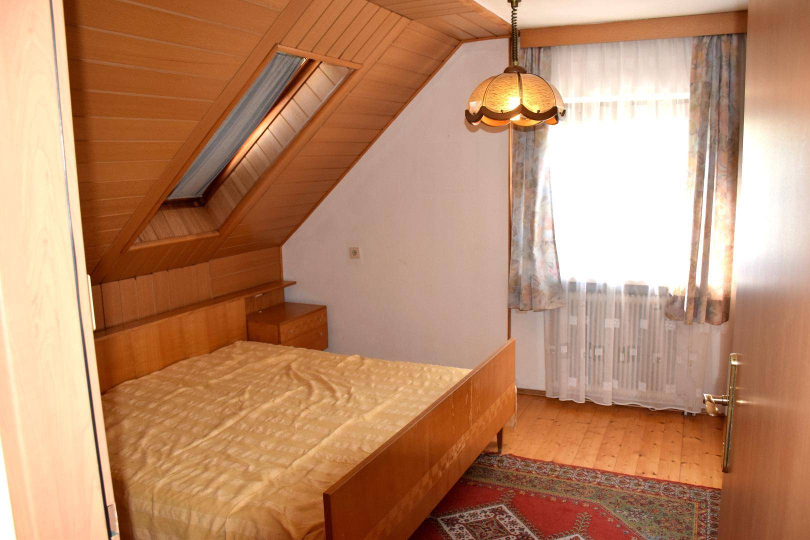 Gemütliches Schlafzimmer im Dachgeschoss mit Holzverkleidung, Bett und Dachfenster.
