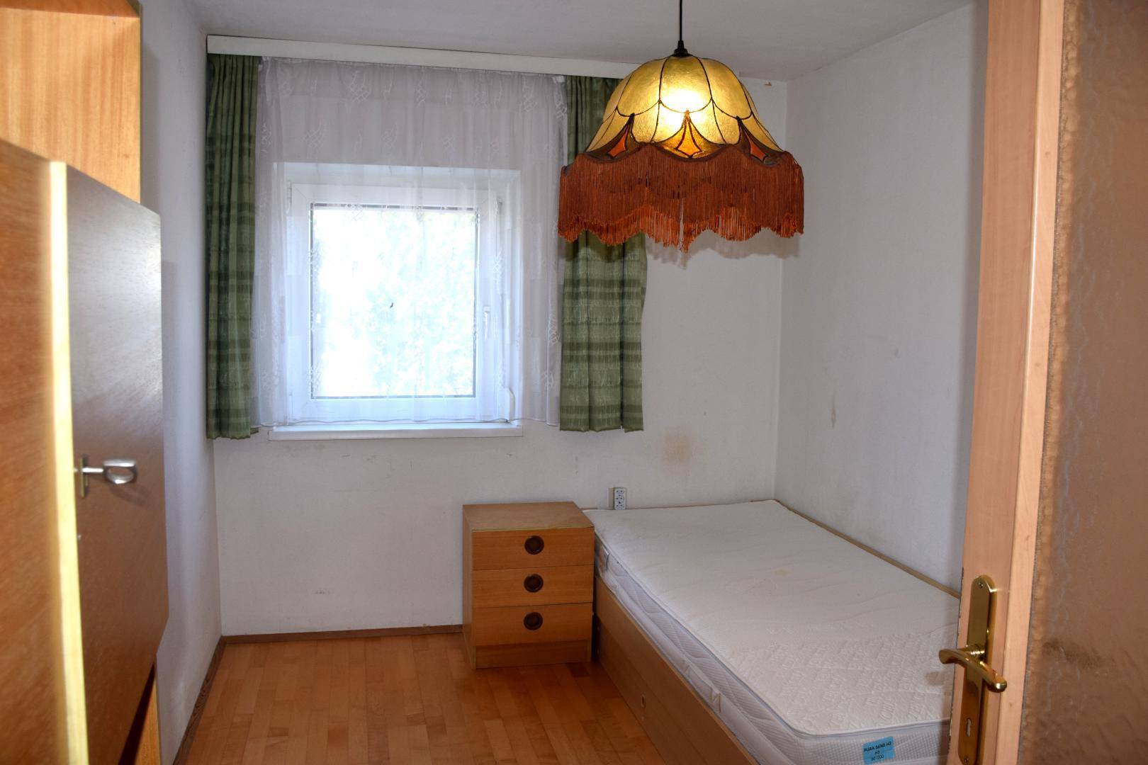 Kleines Schlafzimmer mit Einzelbett, Nachttisch und Fenster, einfach eingerichtet.