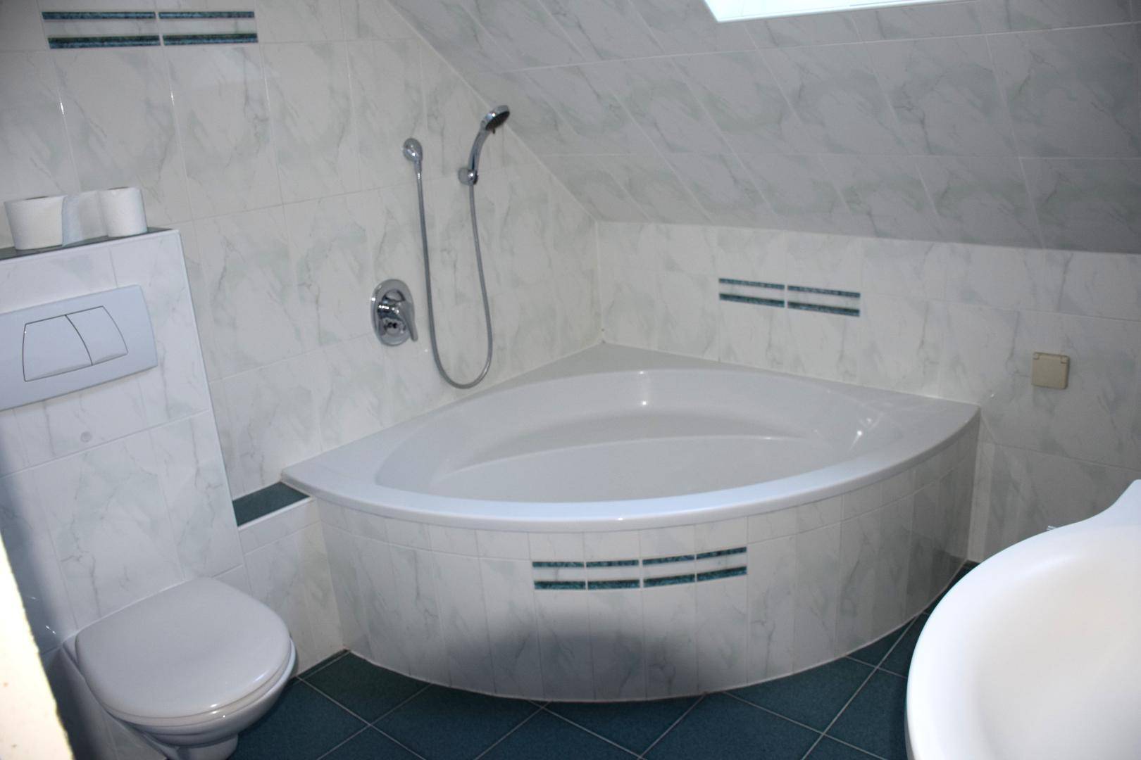 Badezimmer im Dachgeschoss mit Eckbadewanne, WC und hellen Fliesen an Wänden und Boden.