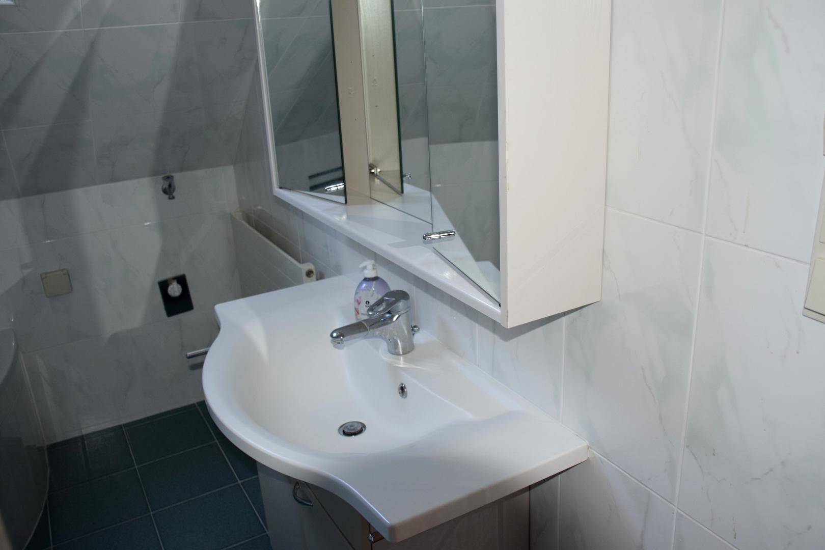 Badezimmer mit Einzelwaschbecken, Spiegelschrank und hellen Fliesen, unter Dachschräge.