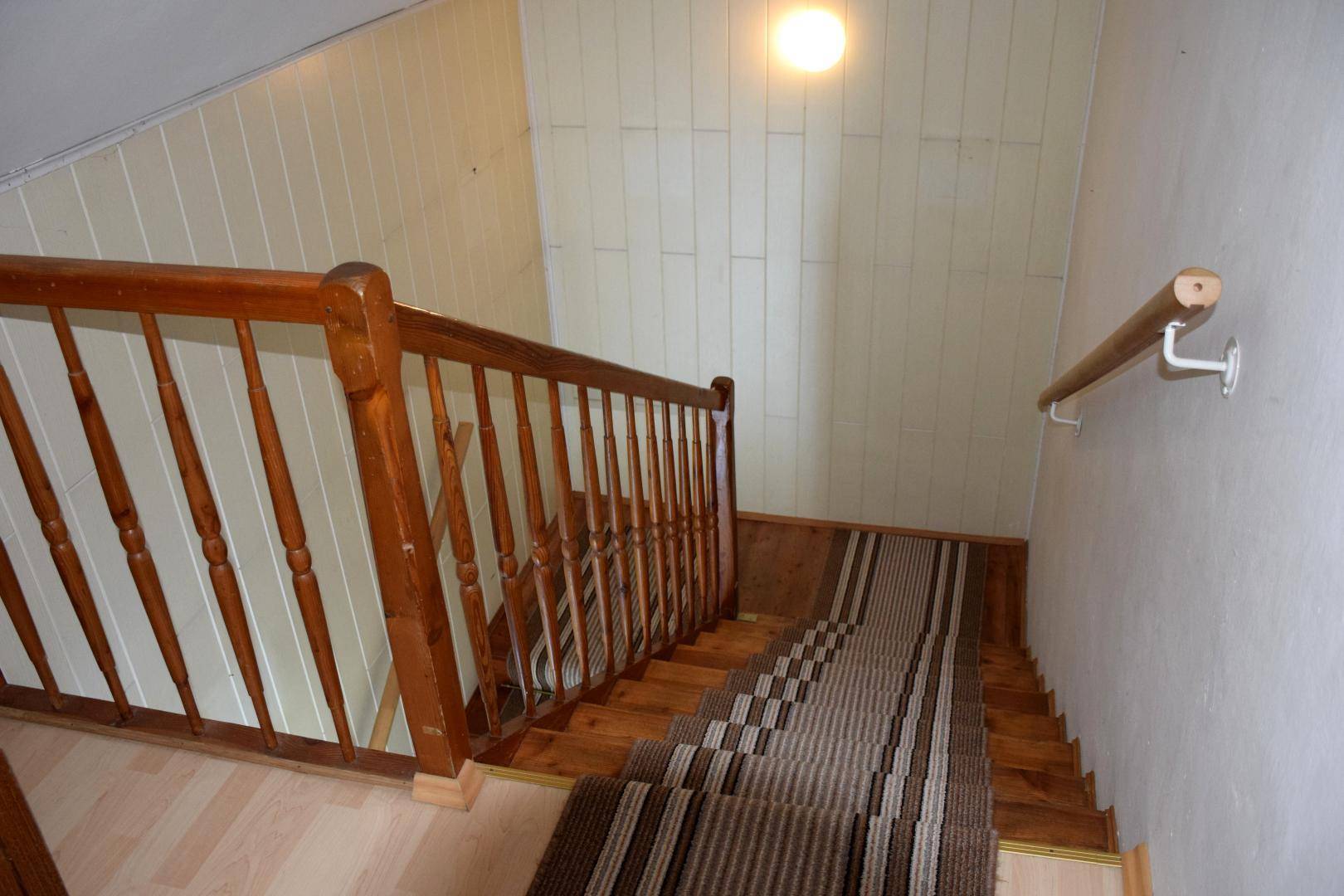 Holztreppe mit Teppichläufer und Holzgeländer, die in das obere Stockwerk führt.