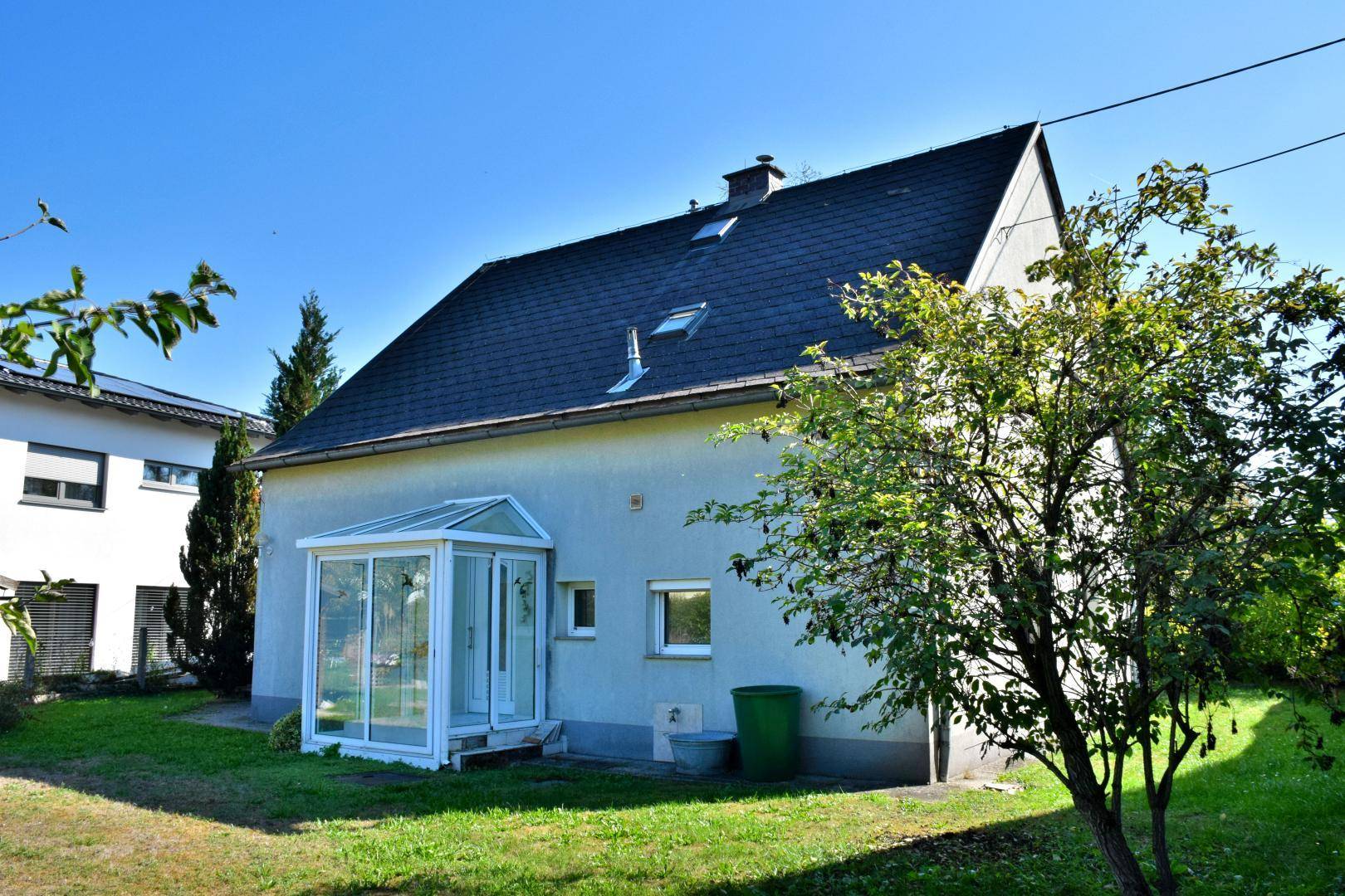 Rückansicht des Hauses mit einem Wintergartenanbau und einem dunklen Satteldach.