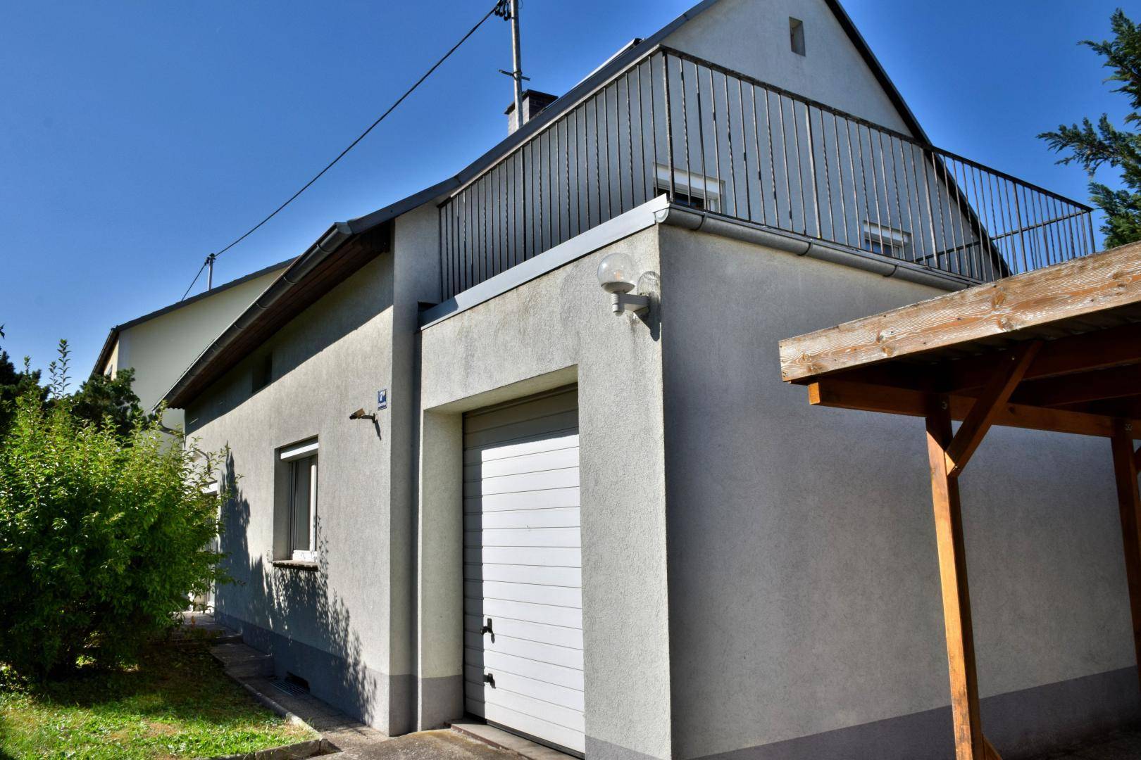 Seitenansicht des Hauses mit Garage, Carport und einem kleinen Balkon im Obergeschoss.