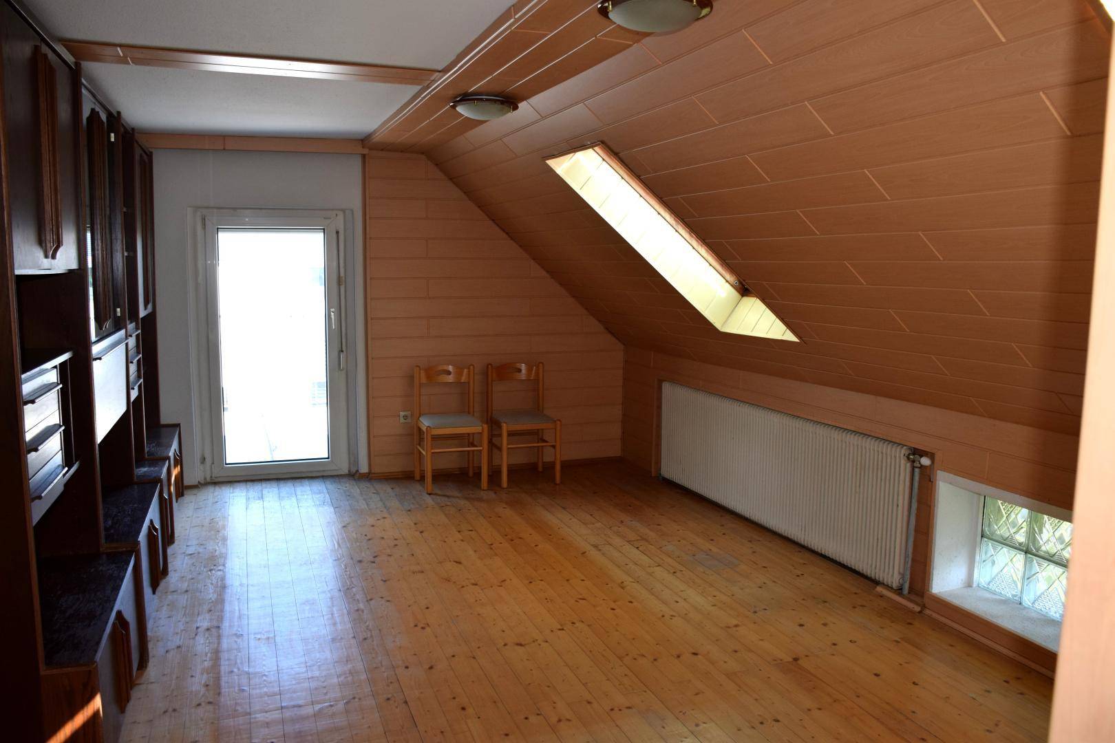Geräumiger Dachbodenraum mit Holzverkleidung, Holzboden und Zugang zu einem Außenbereich.